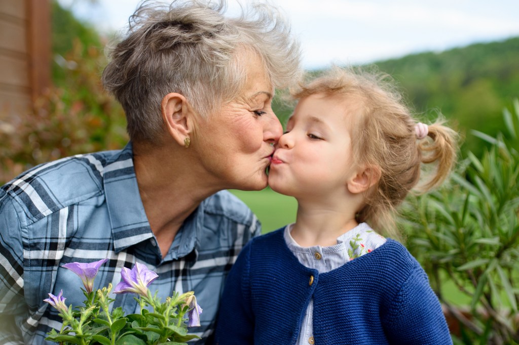 Happy elderly grandmother with little granddaughter gardening on balcony in summer,